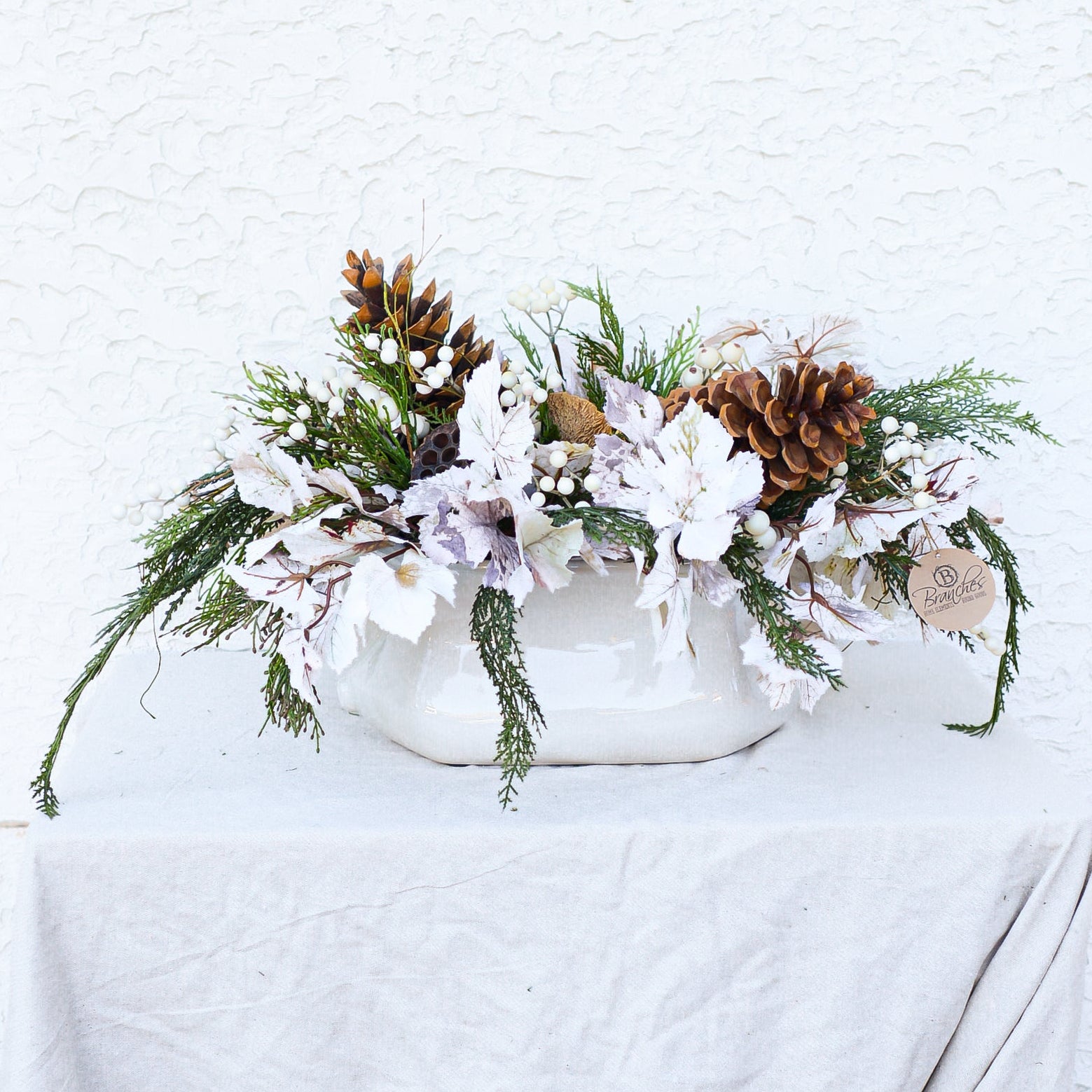 Decorative holiday centerpiece with pine cones frosted leaves and greenery in oversized white container