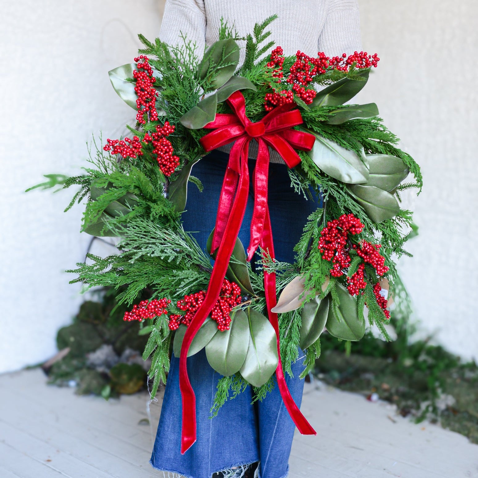 Person holding a large green wreath with red berries and a red ribbon against a white background hilton head island south carolina christmas