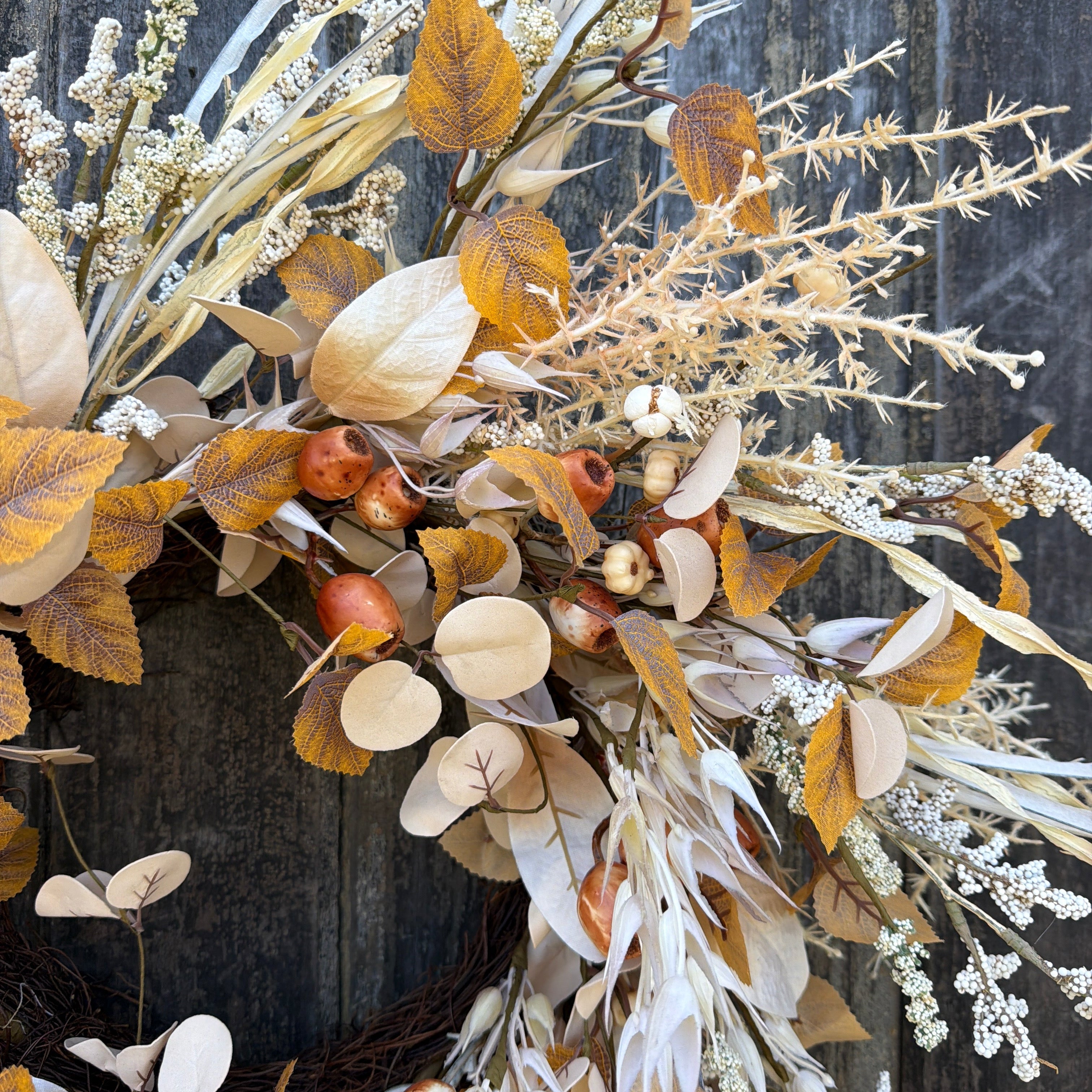 Autumn dried floral wreath with eucalyptus leaves, acorns, and delicate white sprigs on a rustic dark wood background.